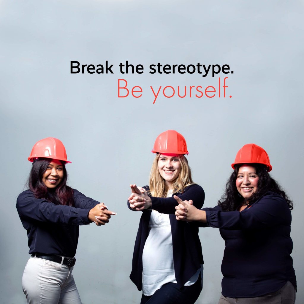 Three women wearing red hard hats and pointing forward stand against a grey background, with the text "Toronto Restoration. Be yourself." above their heads.