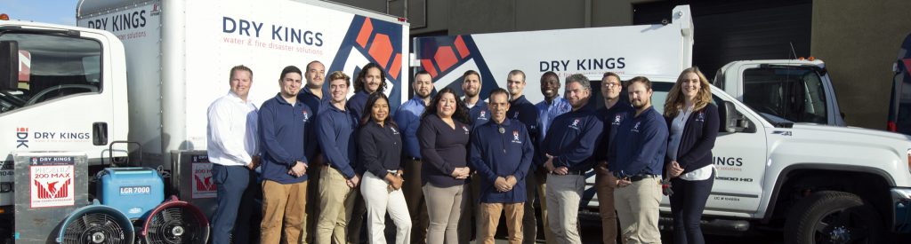 Group of diverse employees standing in front of Toronto Restoration branded trucks outside their facility, dressed in company uniforms.